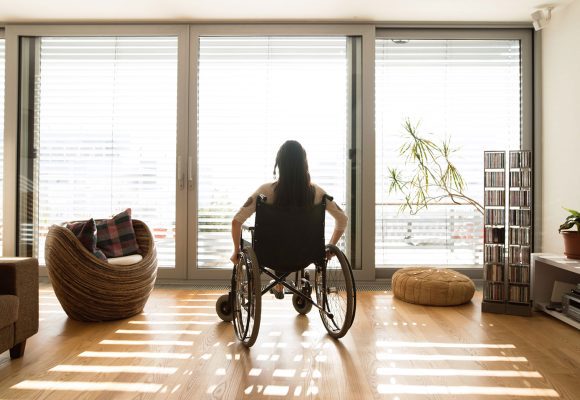 A person sits in a wheelchair by the window of their home