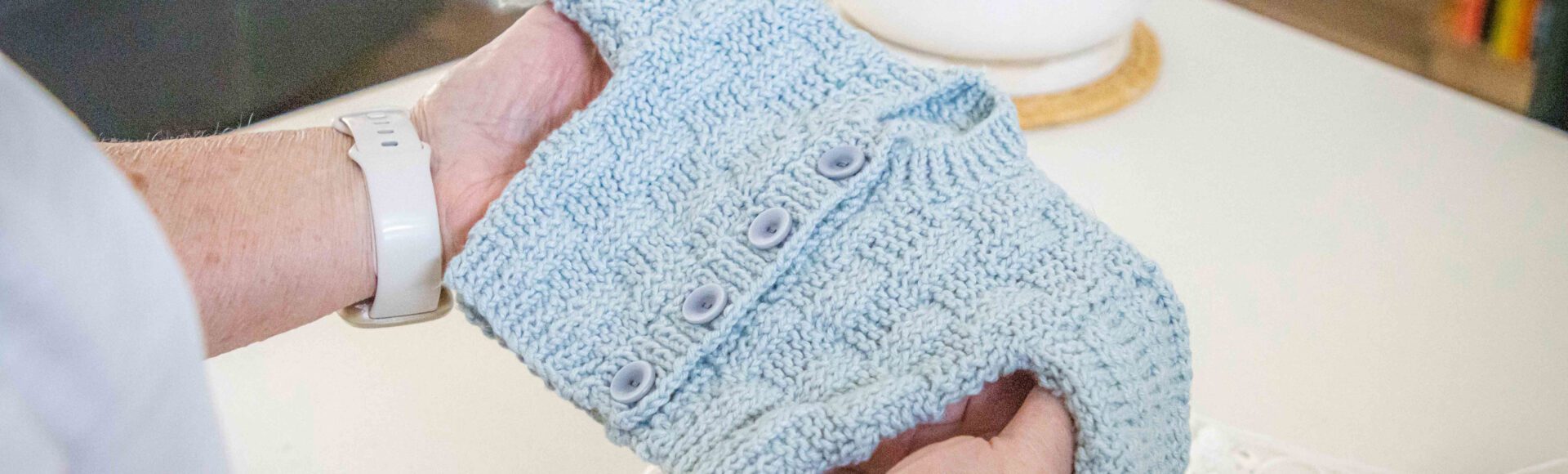 Detail of a woman's hands holding a knitted baby jumper