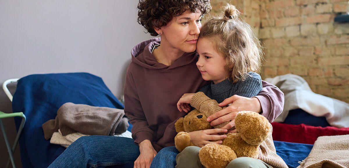 Mother and young daughter sitting on a bed
