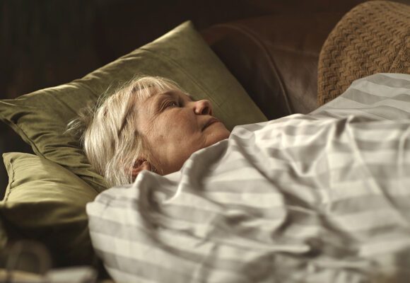 Older woman awake and laying on a couch in the dark