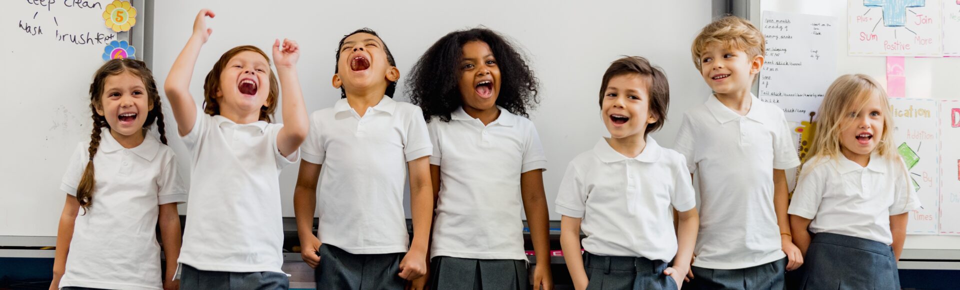 Group of children in school uniforms laughing and smiling in a classroom.