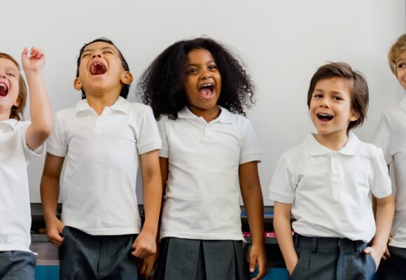 Group of children in school uniforms laughing and smiling in a classroom.