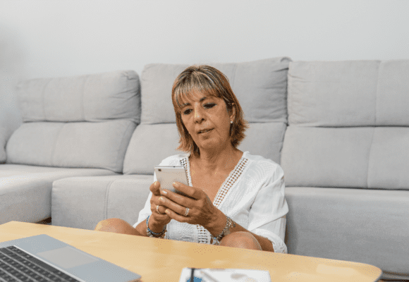 Woman sitting in her living room typing messages from her mobile phone.