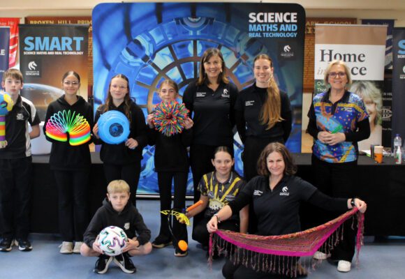 Michelle Faithfull and the University of Newcastle SMART team with students at the front of a classroom, holding science equipment during a Curious Minds STEM session.